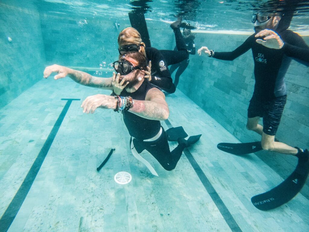 A group practicing freediving techniques underwater in a swimming pool.