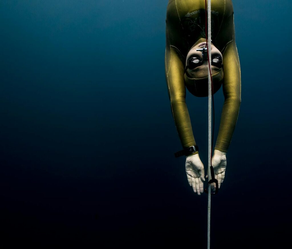 Freediver in wetsuit descends with rope in Bali's blue waters, showcasing underwater exploration.
